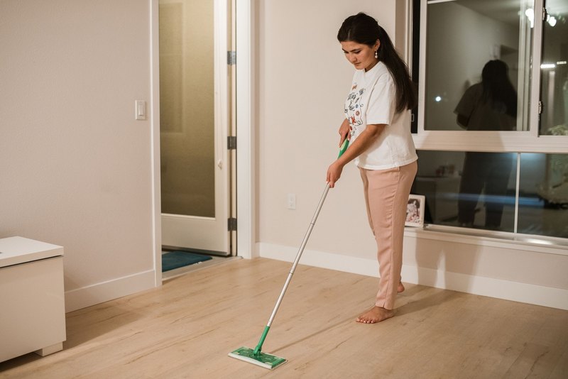 Woman dry-mopping a light wood floor in a bright room