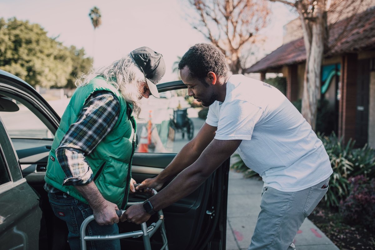 Man steadying the walker of an older man as he steps out of a car