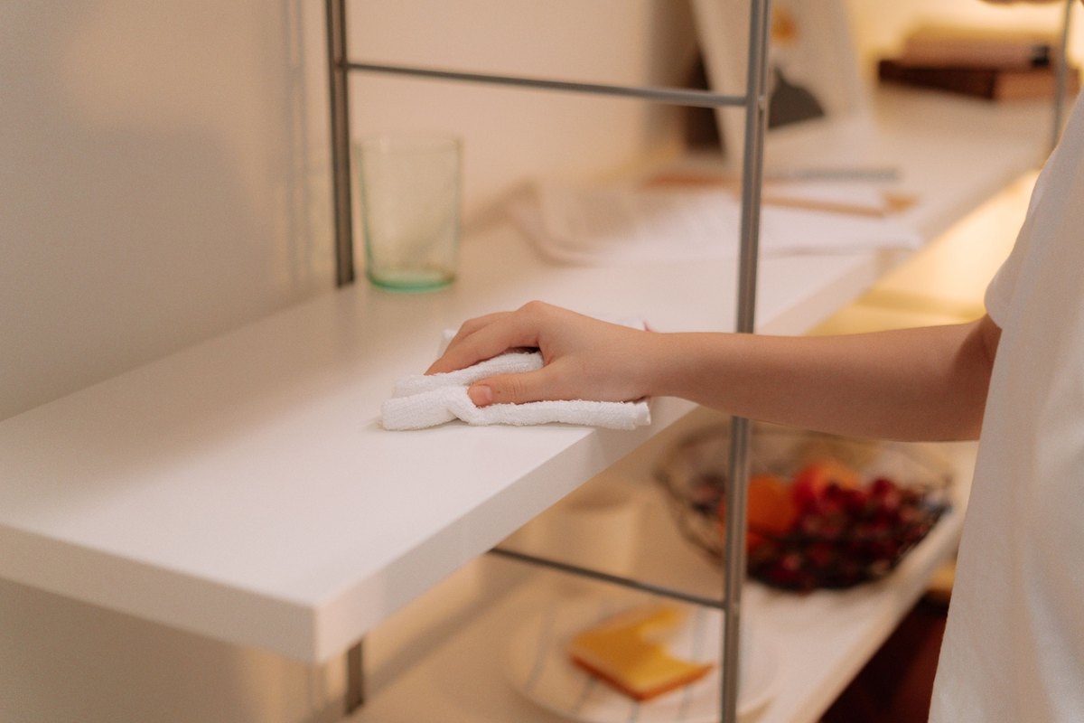 Hand wiping a white shelf with a cloth