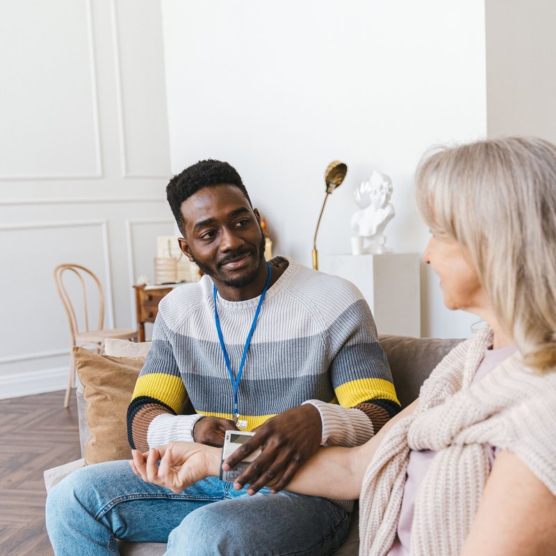 Man with a blue lanyard holding the hand of an older woman beside him on a sofa